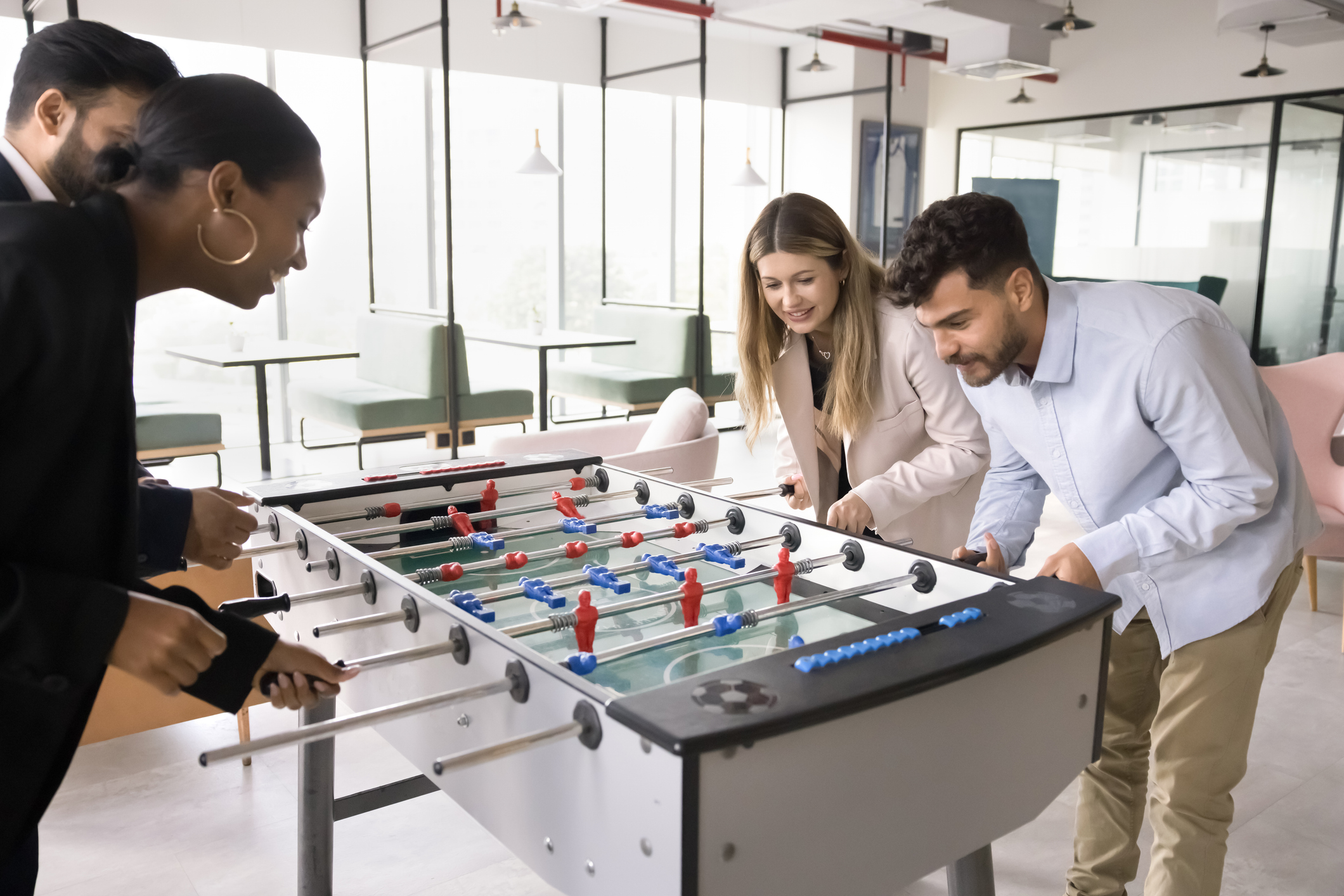 Joyful multiethnic workmates colleagues play foosball match divided into teams